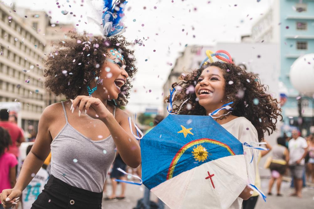 Confeti e duas meninas dançando no carnaval de rua celebando a vitória na Mega Sena de Carnaval